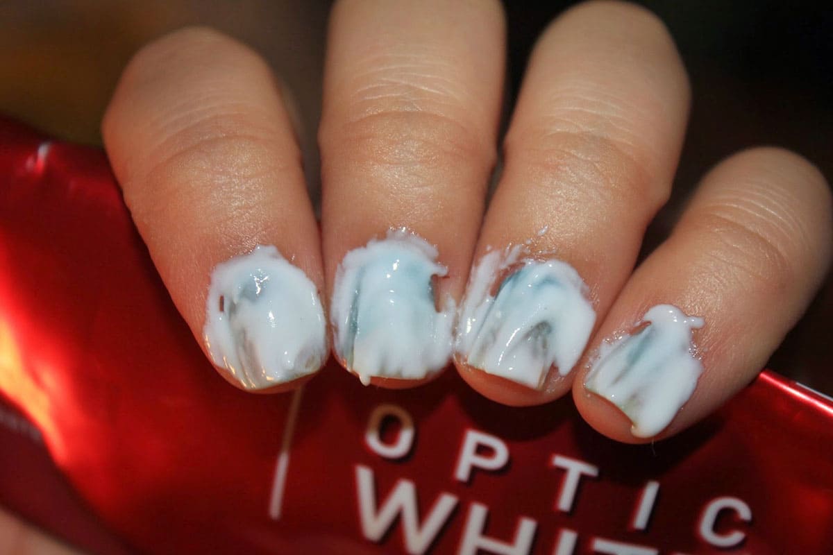 Nails covered in toothpaste and a toothpaste tube