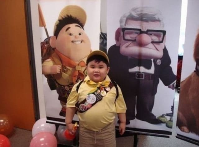 Kid standing next to a poster for Up