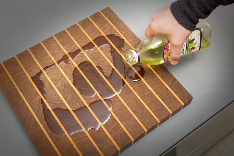 Olive oil being poured onto a used wooden cutting board. 