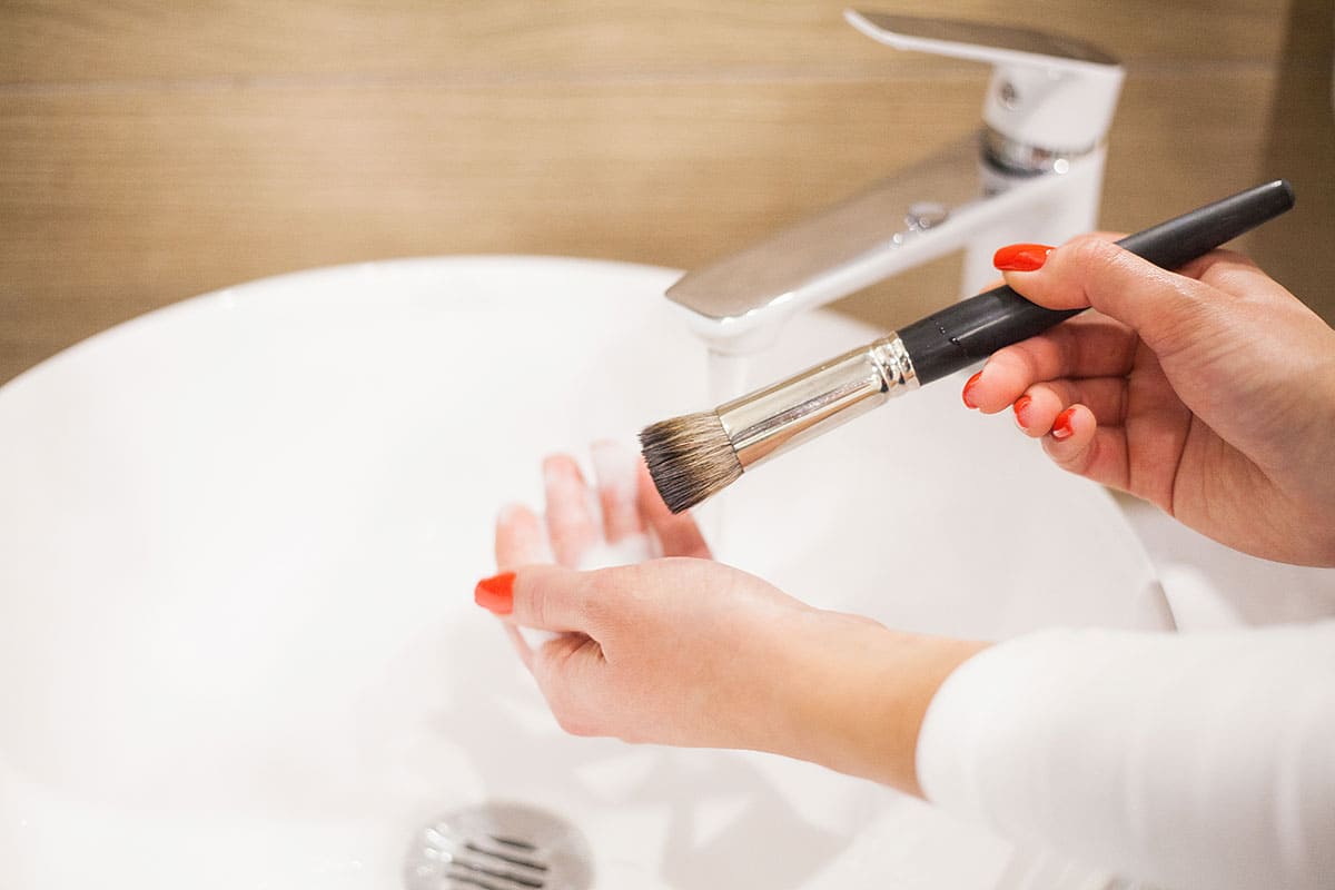 Woman washing dirty makeup brush with soap and oil in the sink.
