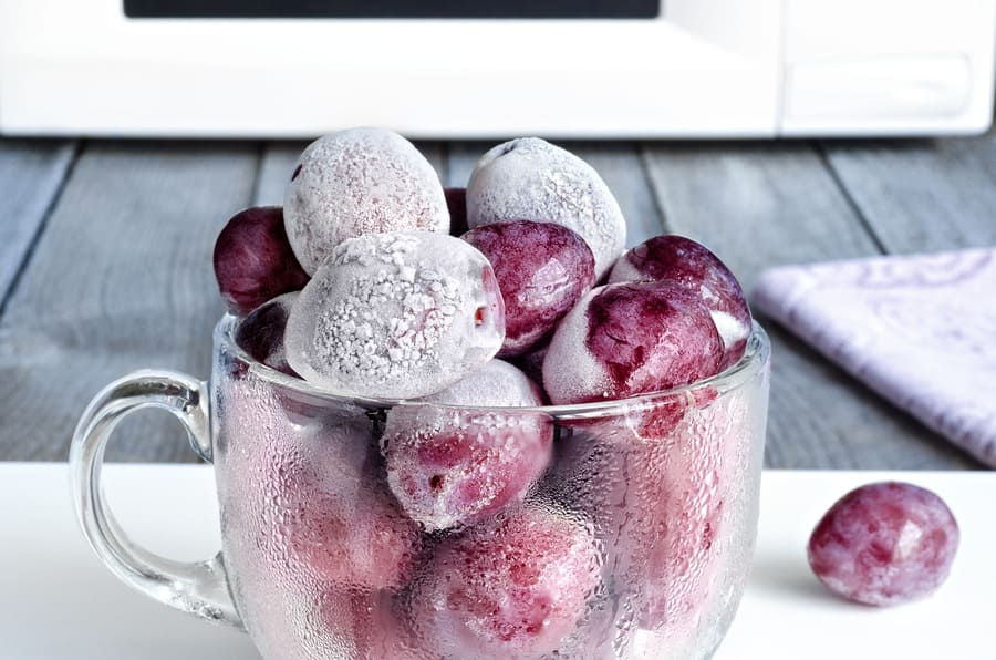 A cup of frozen grapes next to the microwave. 
