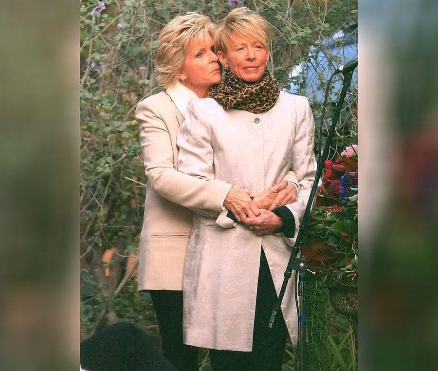 Meredith Baxter and Nancy Locke photographed together as brides on their wedding day with black pants and cream coats. 