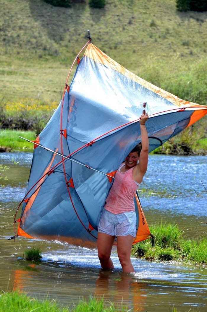 Woman holding up a tent while walking through water 