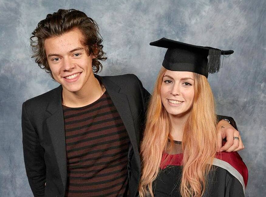 Harry and Gemma Styles are posing with a grey background with Gemma wearing a graduation gown and hat. 