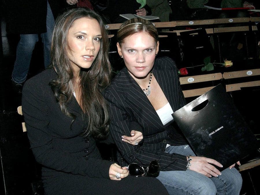 Victoria Beckham and Louise Adams are sitting together linking arms. 