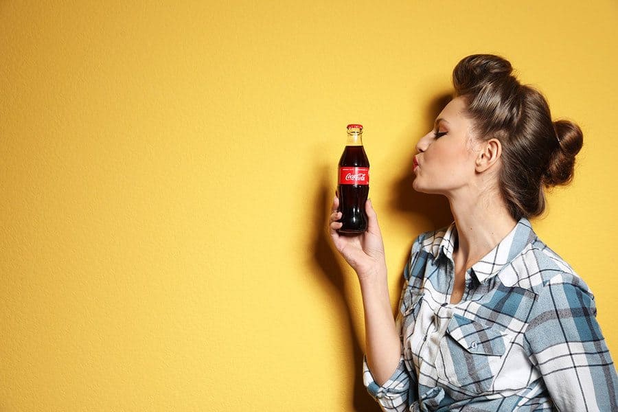 Young woman with bottle of Coca-Cola on color background