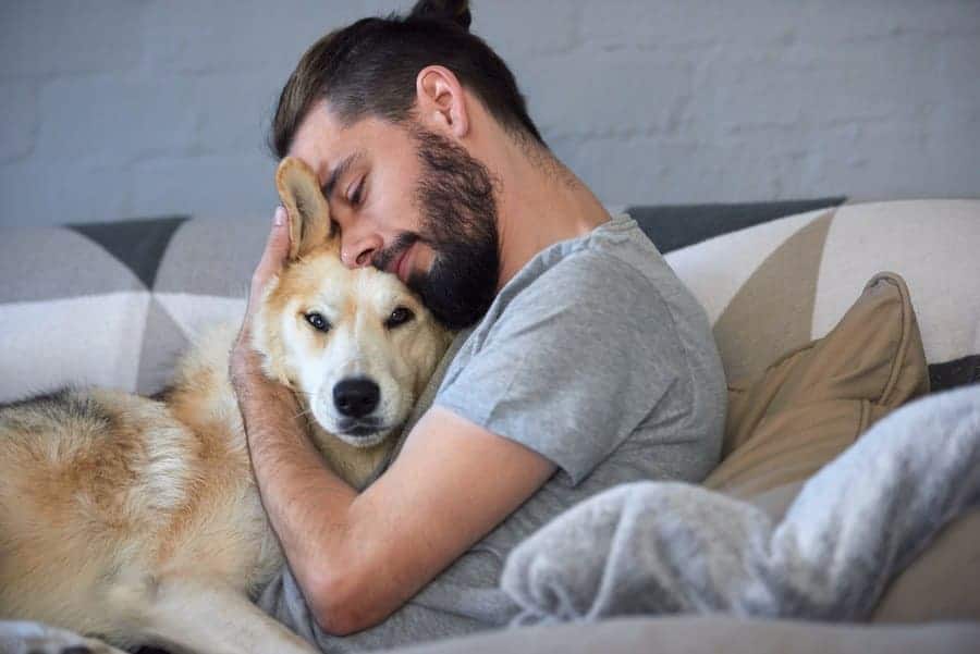 A man is cuddling his dog on the couch. 