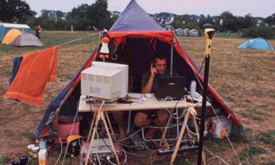 Man in a tent with a desk and computers, talking on the phone 