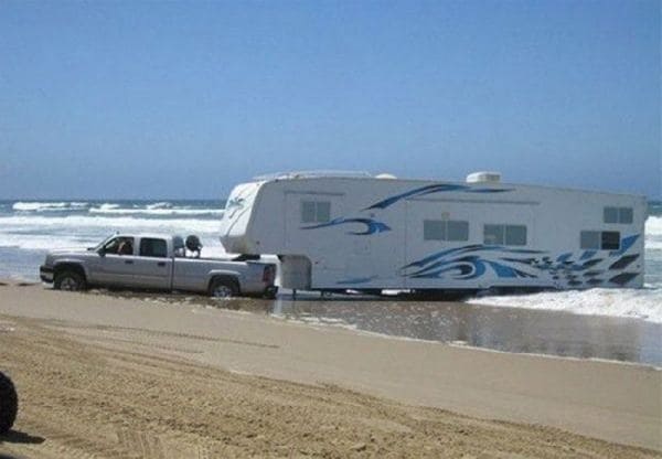truck pulling an RV parked on the beach in the water