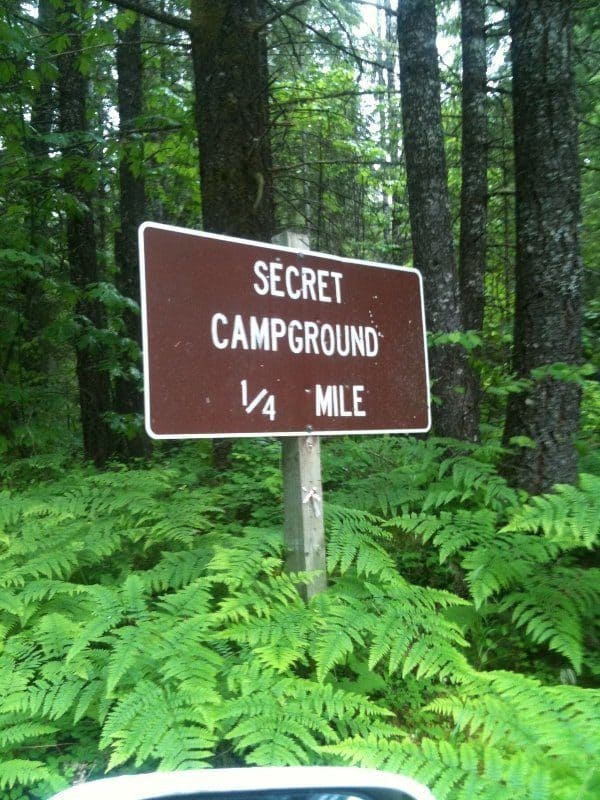 sign in the woods that reads “secret campground ¼ mile.”