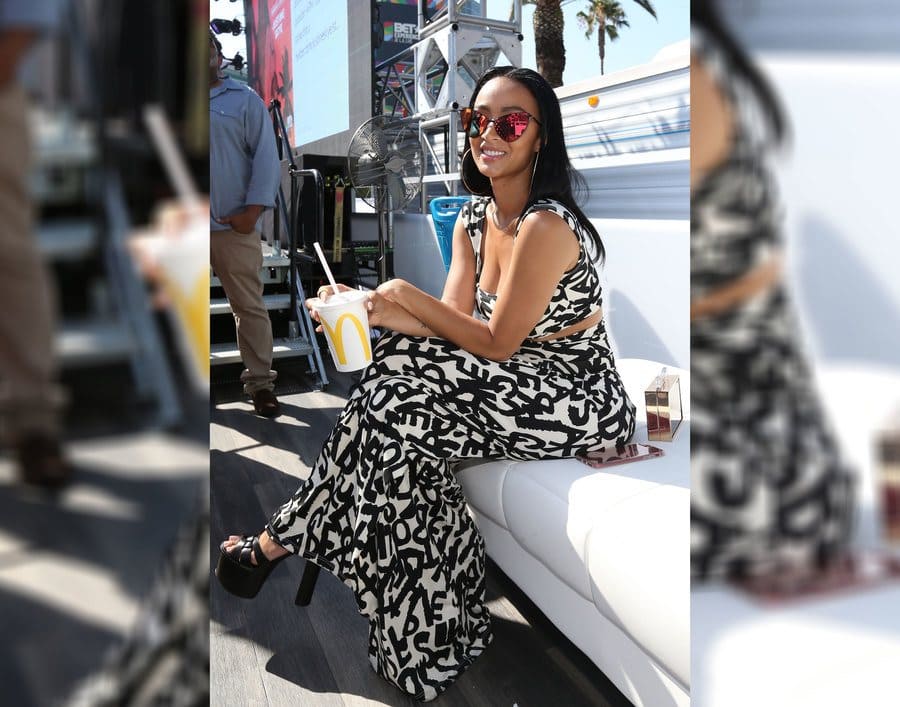 Draya Michele in a two-piece white and black outfit with large chunky black heels and winged sunglasses. 