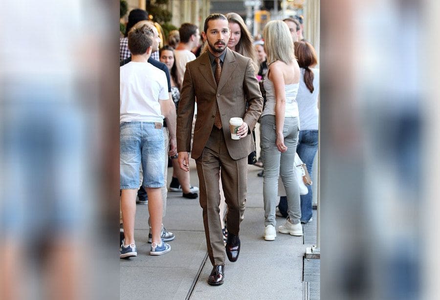 Shia LaBeouf is walking around in a brown suit holding a Starbucks latte. 