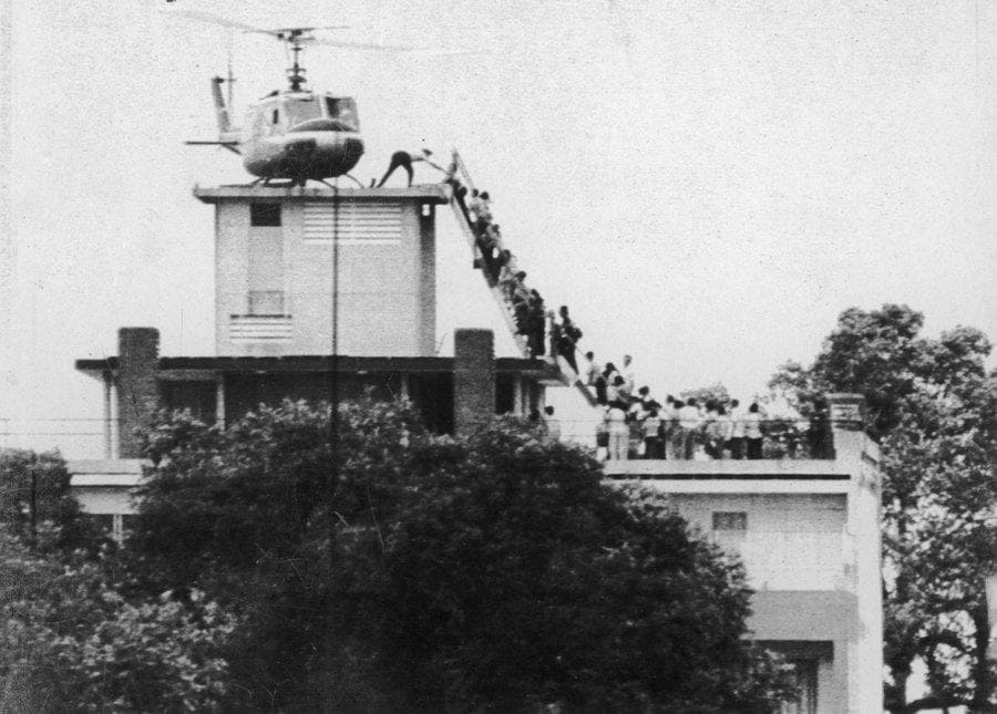 A helicopter on top of a building and people waiting to get on 