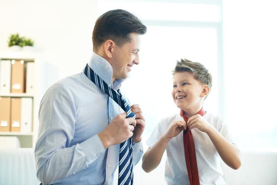 Photo of a happy boy and his father tying neckties
