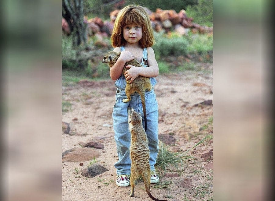 The young girl playing with two meerkats at the age of six in a magical image taken in Namibia