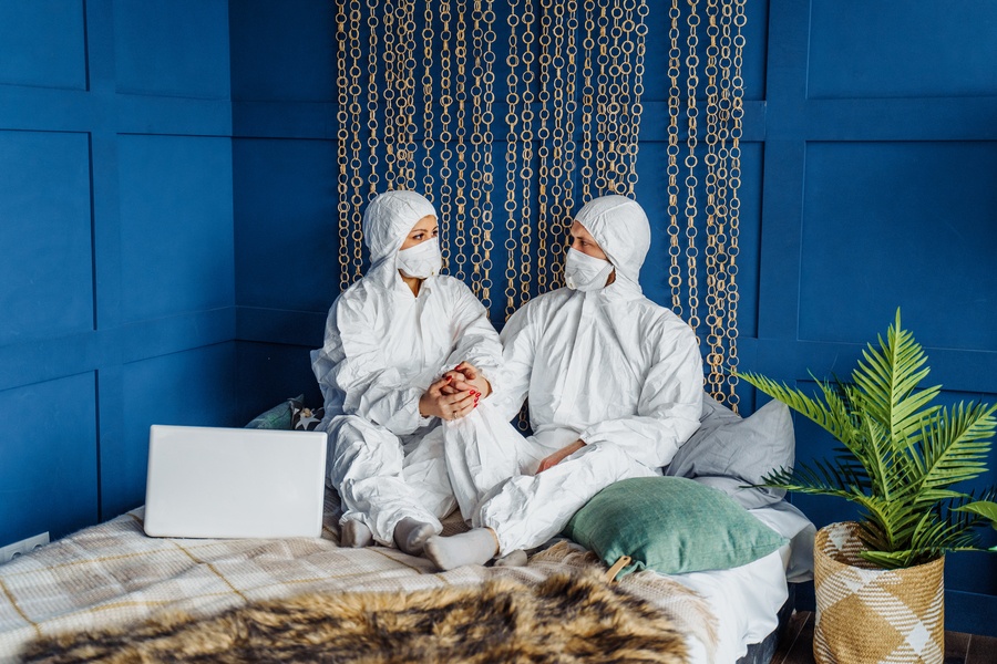 Two people in full white suits and masks on a date in bed. 