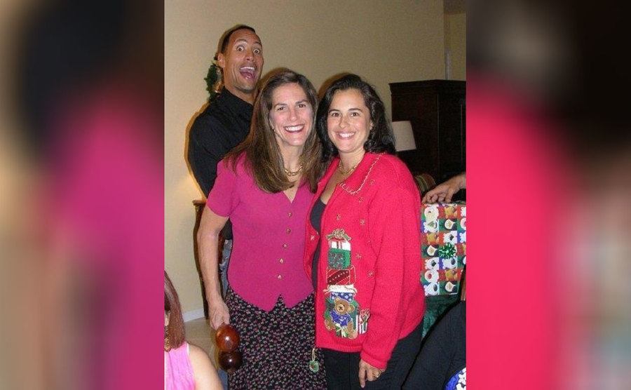 Dwayne Johnson behind two friends posing for a photograph 