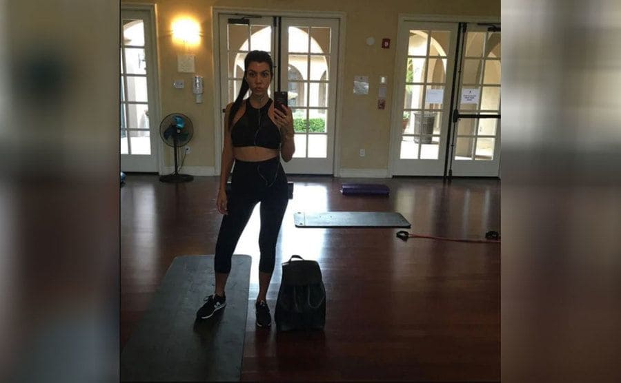 Kourtney Kardashian taking a selfie in the mirror standing on a mat 