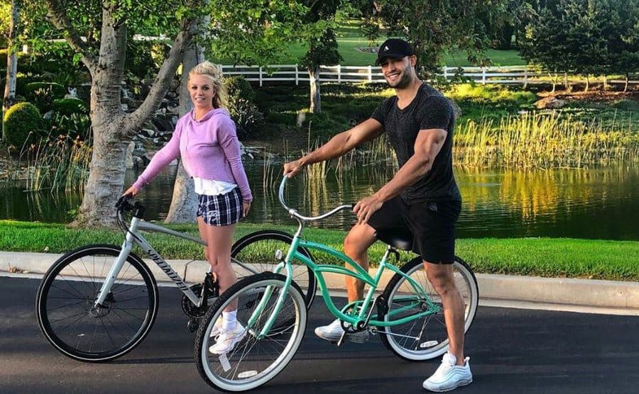 Britney Spears and Sam Asghari riding bikes in front of a small man-made lake in her neighborhood 