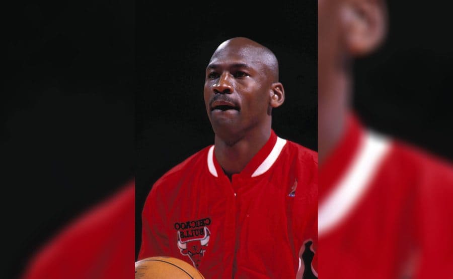 Michael Jordon wearing the Chicago Bulls team jacket and holding a ball with a look of concentration on his face 
