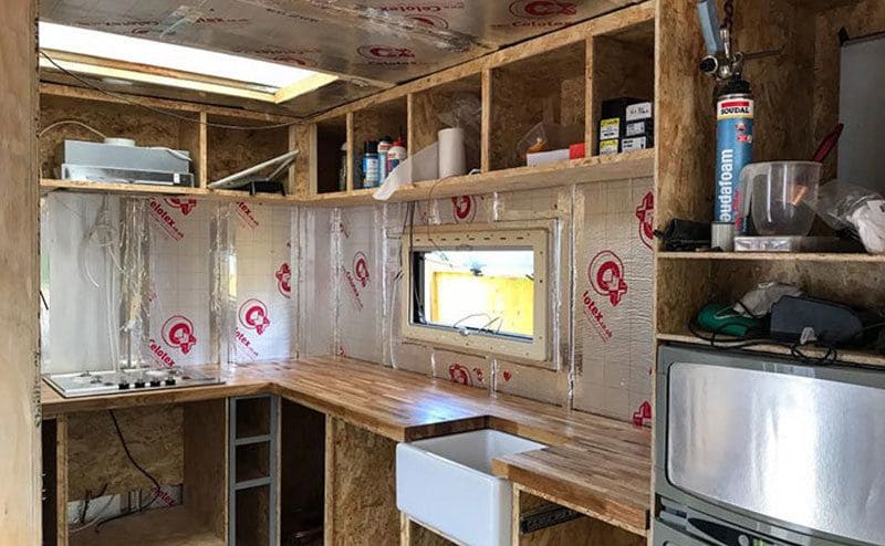 The mobile home kitchen with an oven, sink, and stovetop, and wood and insulation all over. 