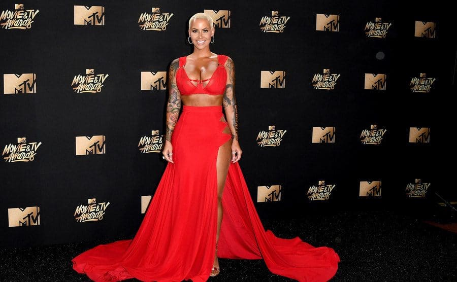 Amber Rose in a long red skirt with a slit, and a small strapped v-neck crop top 