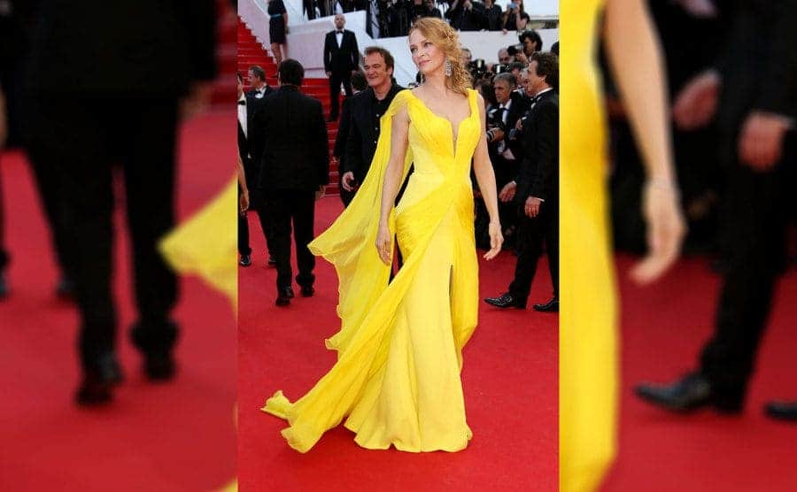 Uma Thurman in a long flowing yellow silk sleeveless dress with a slit in the front and a long train 