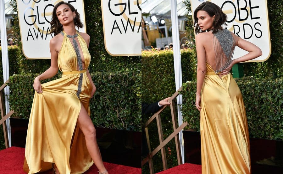 Emily Ratajkowski is wearing a yellow silk halter dress with a silver accent in the center of the plunging neckline and a slit up to her leg / A detailed photograph of the open back of the dress with silver studded chains draping across 