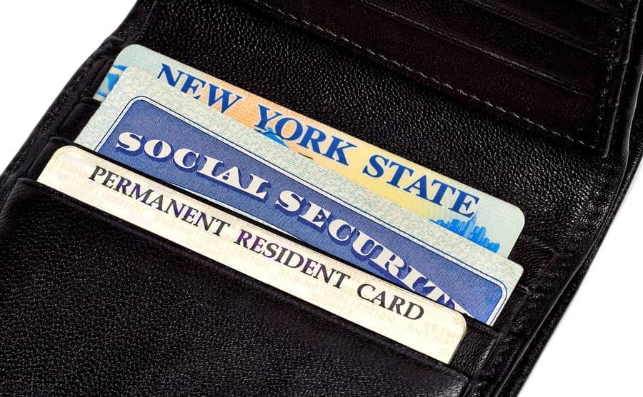 A New York State ID with a social security card and permanent resident card inside of a wallet 