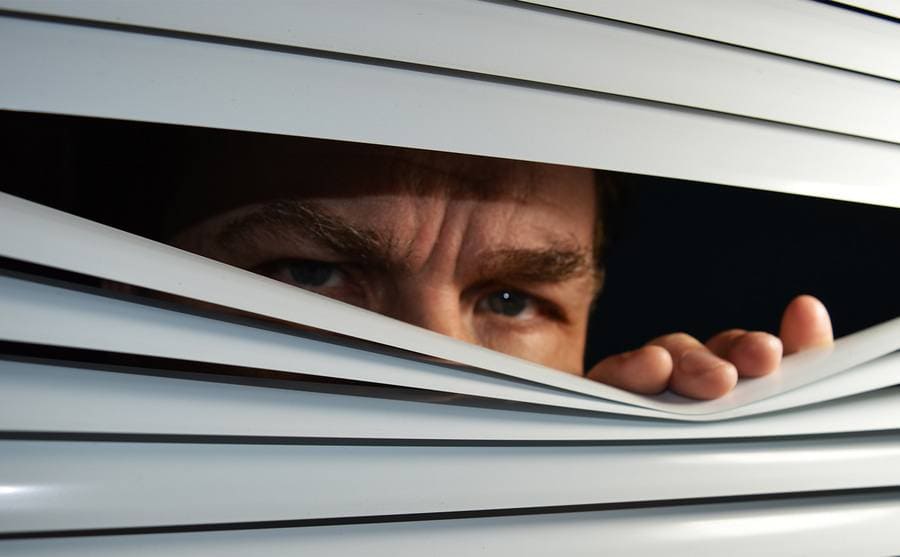 A man looking through blinds