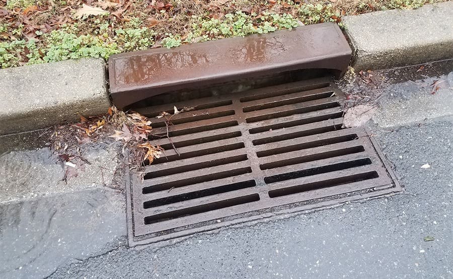 A metal storm drain with water running into it 