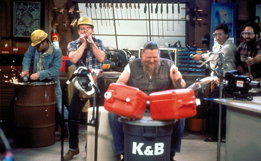 Tim Allen, Richard Karn, Gary McGurk, Casey Sanders, and Mickey Jones playing tools like instruments in the garage in Home Improvement 