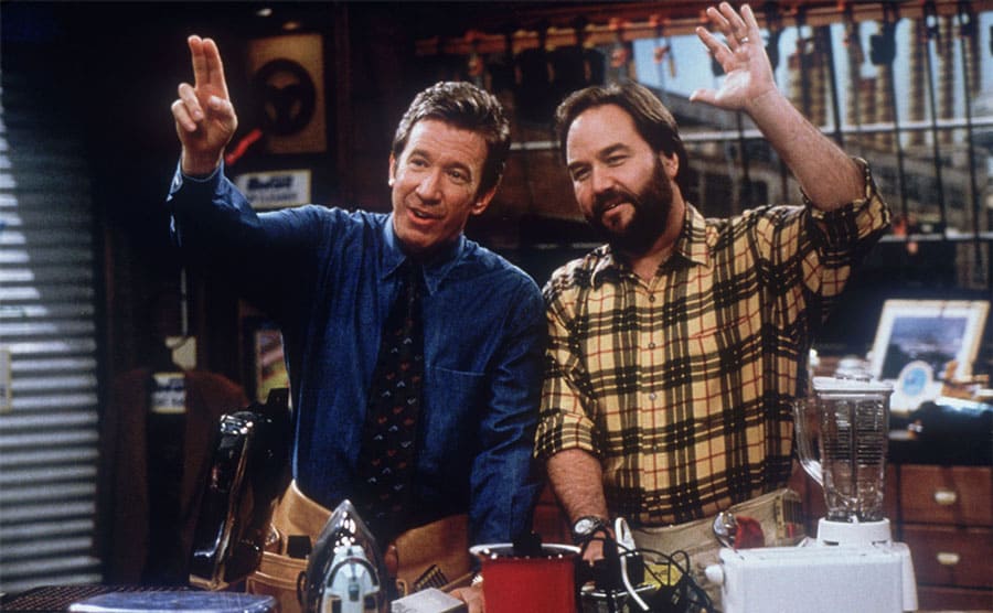 Tim Allen and Richard Karn with kitchen electronics on the table in front of them 