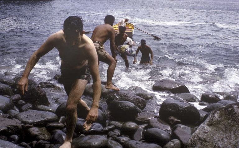 Boys climbing rocks onto shore 