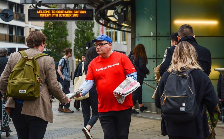 A man handing out newspapers at a train station 
