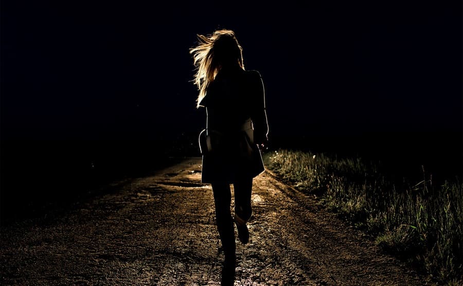 A girl running on a road with the headlights of a car behind her 
