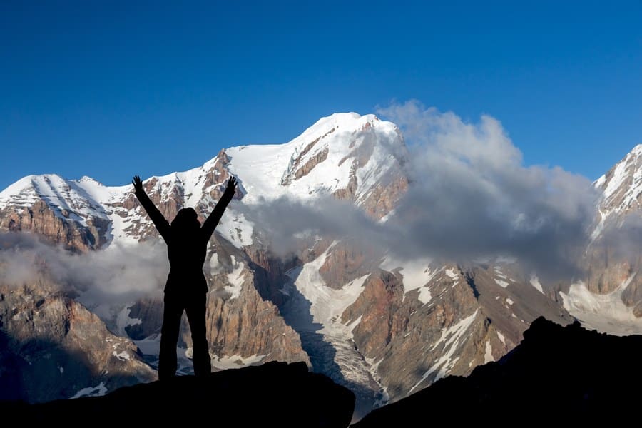 A woman standing triumphantly on the top of a rocky cliff. 
