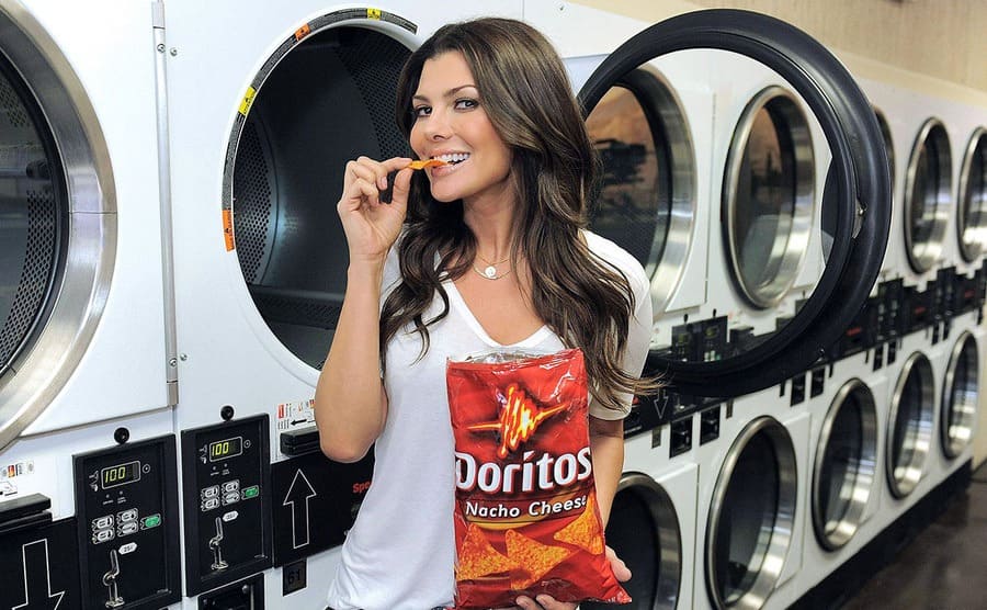 Ali Landry eating Doritos while standing in front of a washing machine for a commercial 