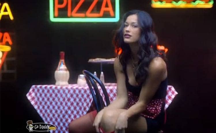 Rachelle Wood in the Go Daddy commercial sitting at a table with a pizza sitting on it 