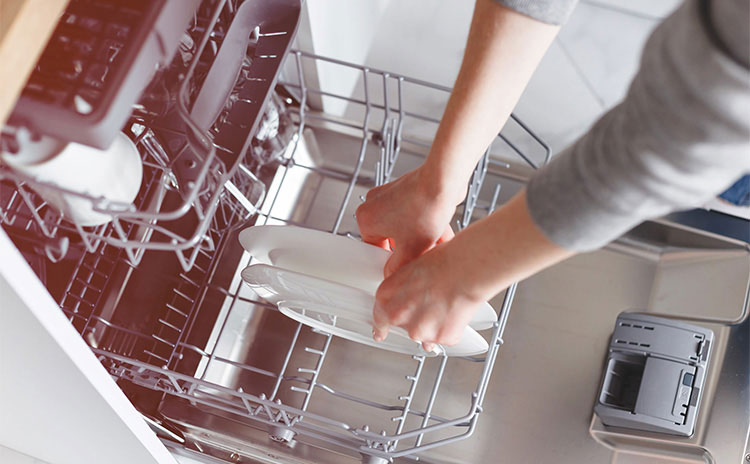 A woman placing washed dishes in the dishwasher to dry 