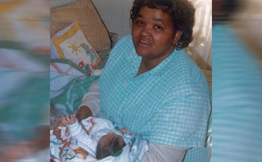 Lavona holding Miché as a baby while sitting on a bed 
