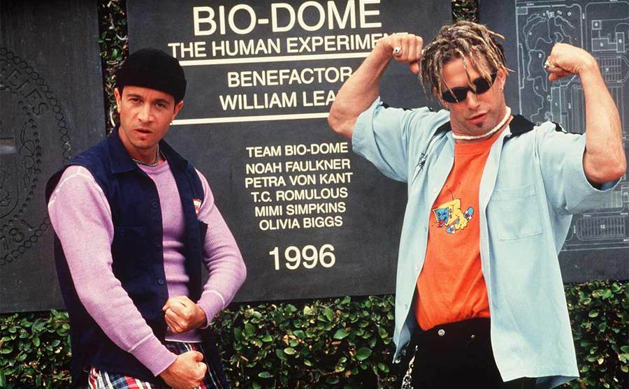 Pauly Shore and Stephen Baldwin standing in front of a sign for the Bio-Dome human experiment with Stephen flexing his arms 