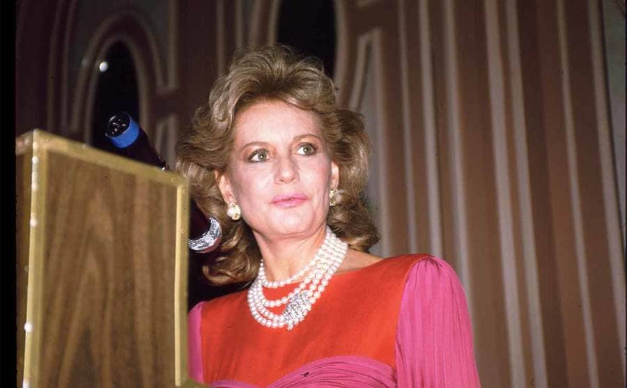 Barbara Walters at an event wearing a pink and red dress with pearls 