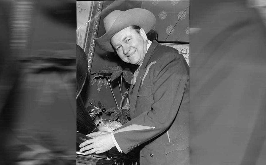 Tex Ritter standing next to a Gramophone wearing a cowboy hat