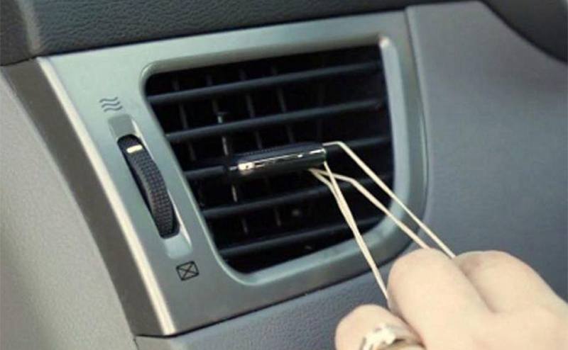 A person putting a rubber band around the air conditioning vent in a car 