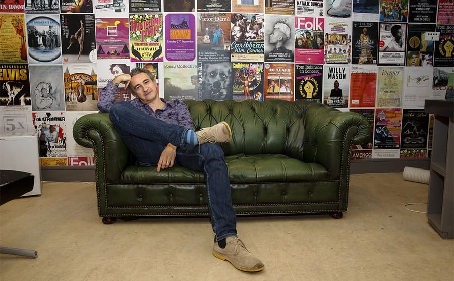 Simon Garfield sitting on a green couch in front of a wall of posters