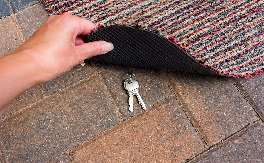 A woman lifting a doormat to reveal hidden keys 