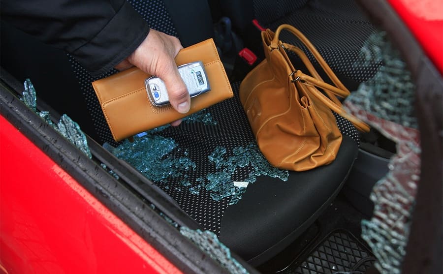 Someone reaching into a broken car window taking a wallet and cell phone from a purse left unattended 
