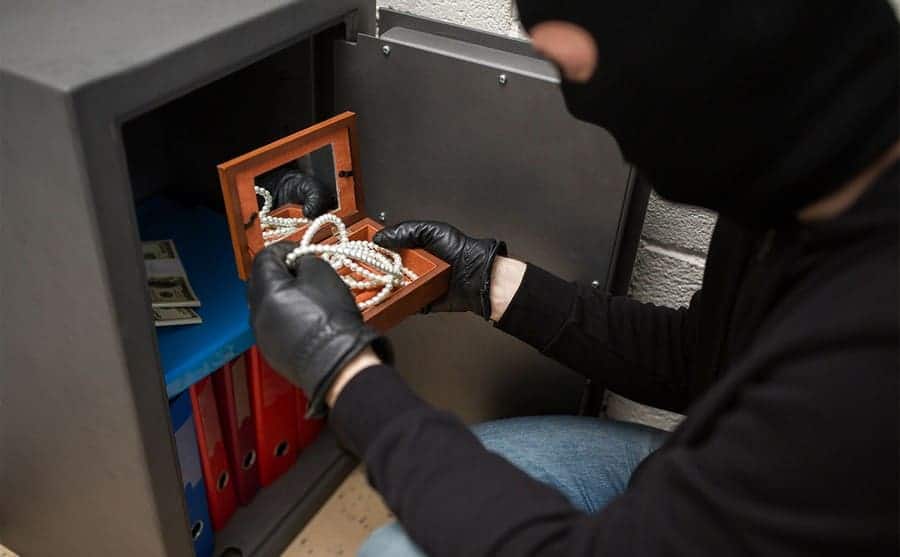 A thief looking through a safe in a home 