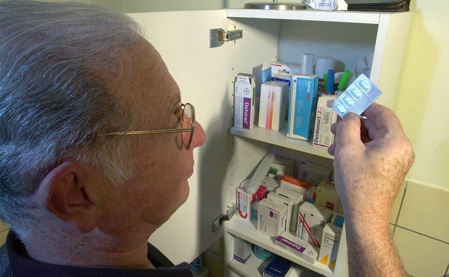 An elderly man taking pills out of a medicine cabinet 